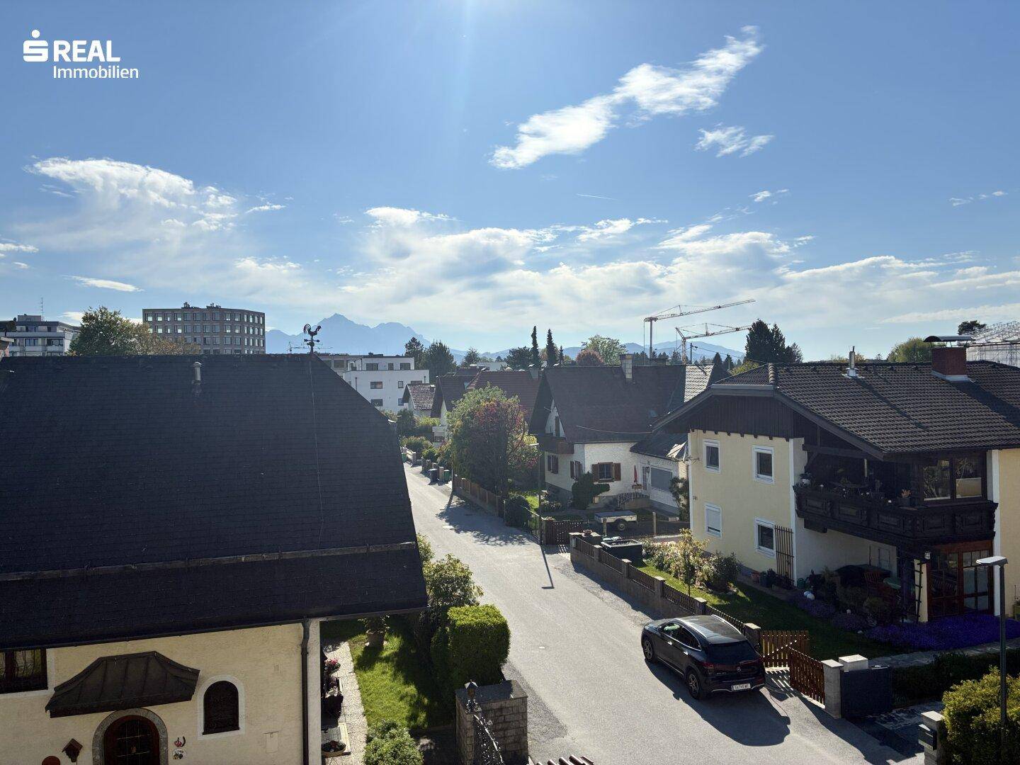 Weitblick über die Wohngegend mit Straße, Häusern und Bergen am Horizont an einem sonnigen Tag.