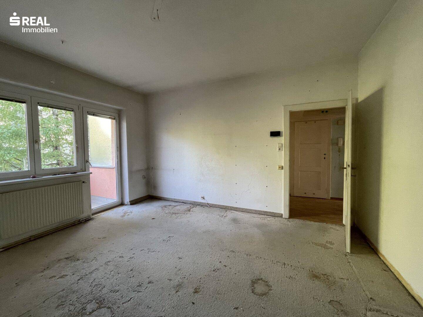Helles Wohnzimmer mit Balkonzugang und renovierungsbedürftigem Zustand, ideal für individuelle Gestaltung.
