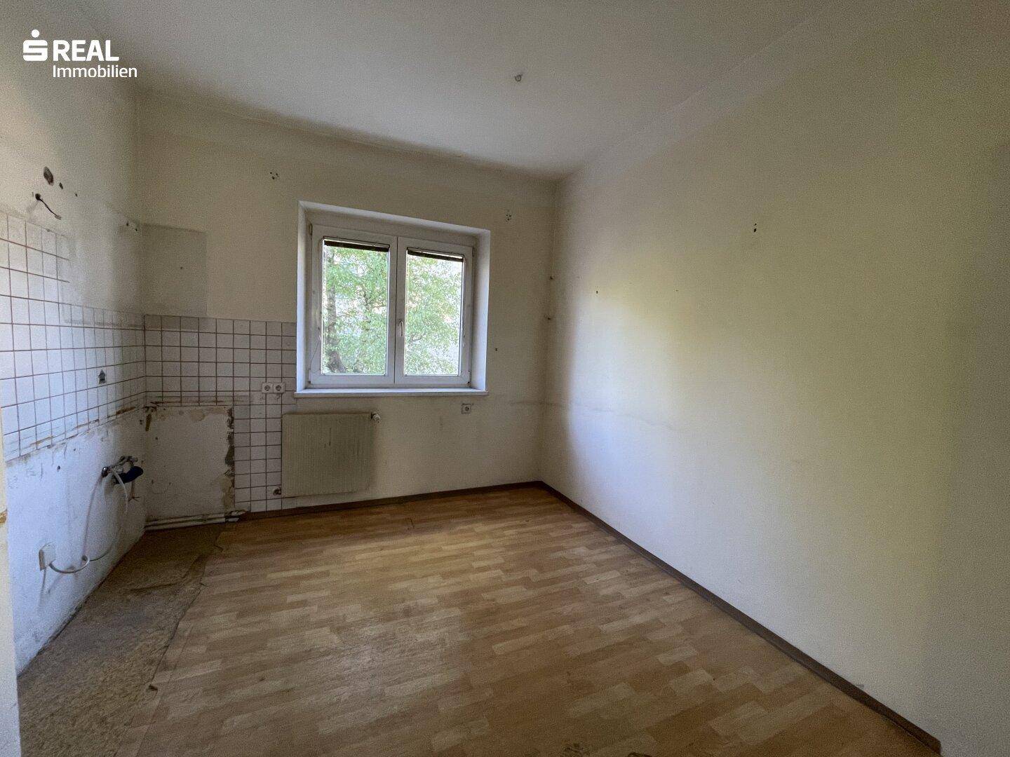 Küche mit gefliester Wand und Fenster, bereit für die Installation einer neuen Einbauküche.