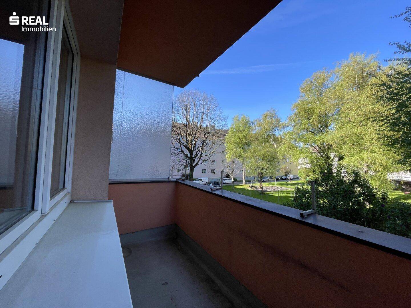 Sonniger Balkon mit Blick ins Grüne und auf die umliegenden Wohngebäude.