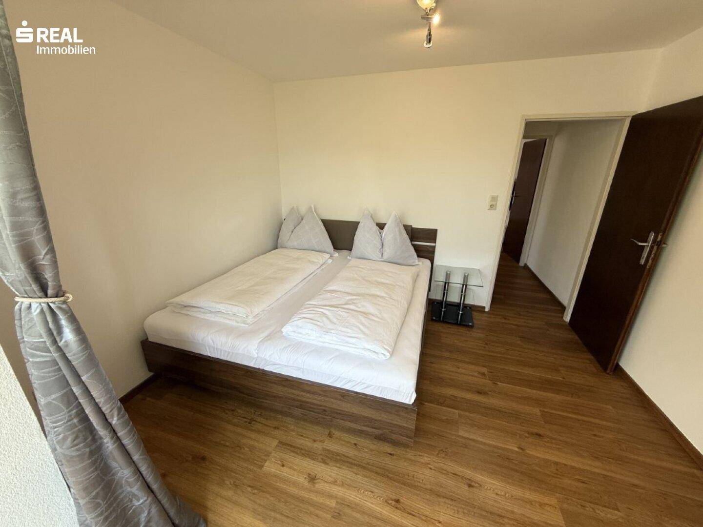 Helles Schlafzimmer mit Doppelbett und Laminatboden.