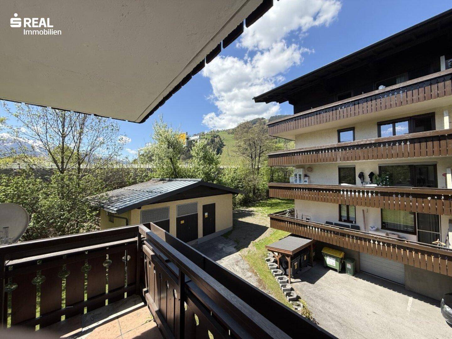 Blick vom Balkon auf die umliegenden Gebäude und die grüne Umgebung mit Bergen im Hintergrund.