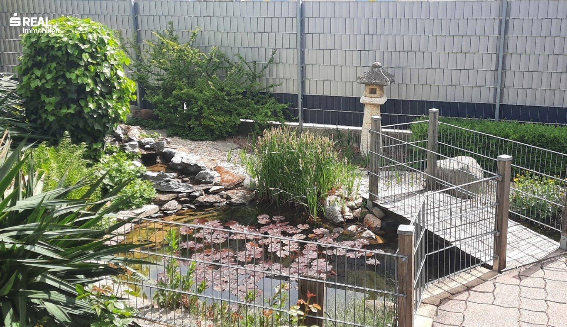 Idyllischer Gartenteich mit Seerosen, kleiner Brücke und japanischer Steinlaterne.