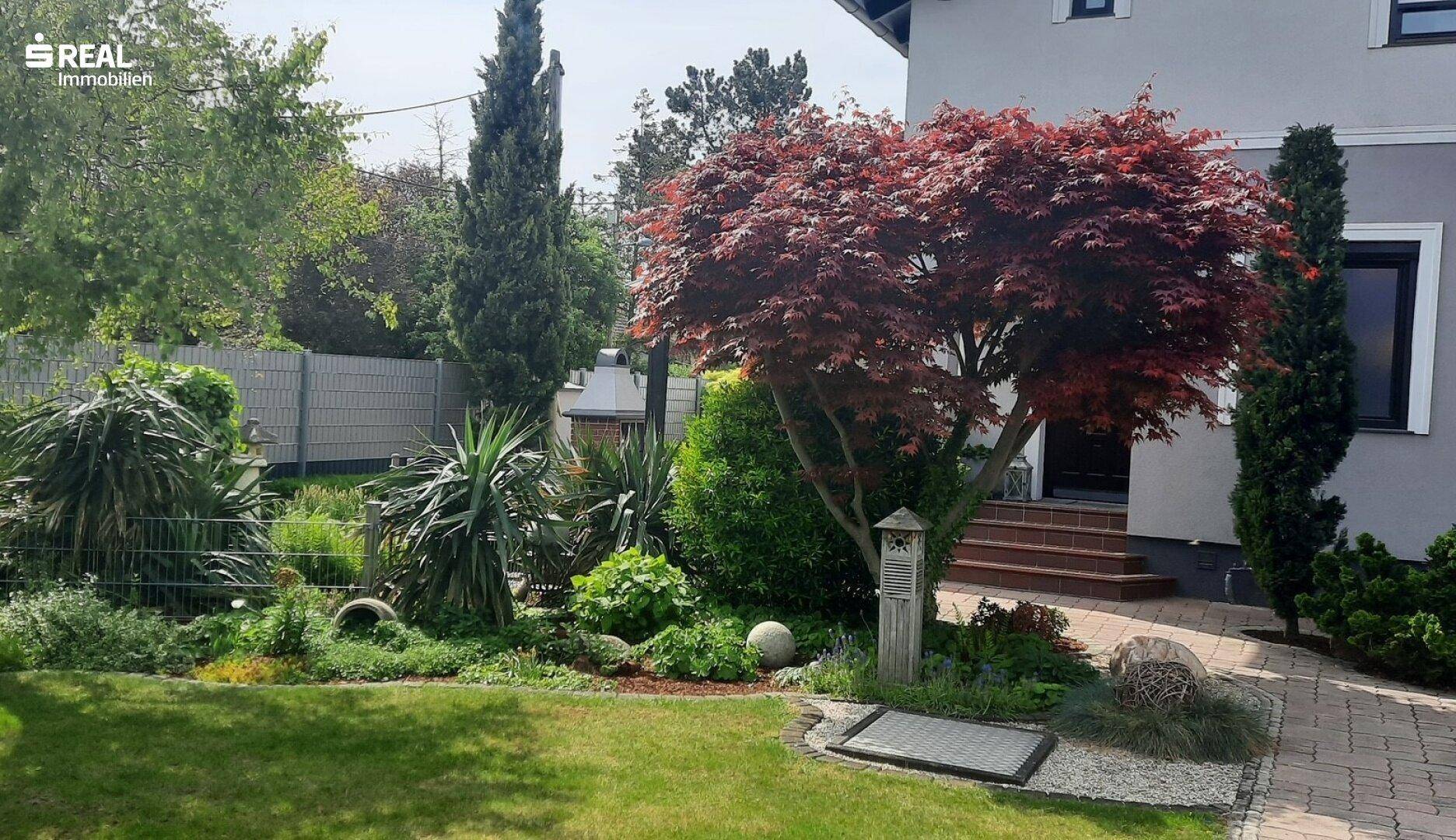 Weitläufiger Garten mit vielfältiger Bepflanzung und gepflastertem Weg zum Hauseingang.