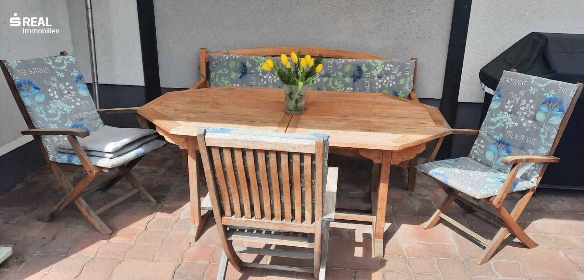 Gemütliche Terrasse mit Holztisch und Stühlen, ideal für Mahlzeiten im Freien.