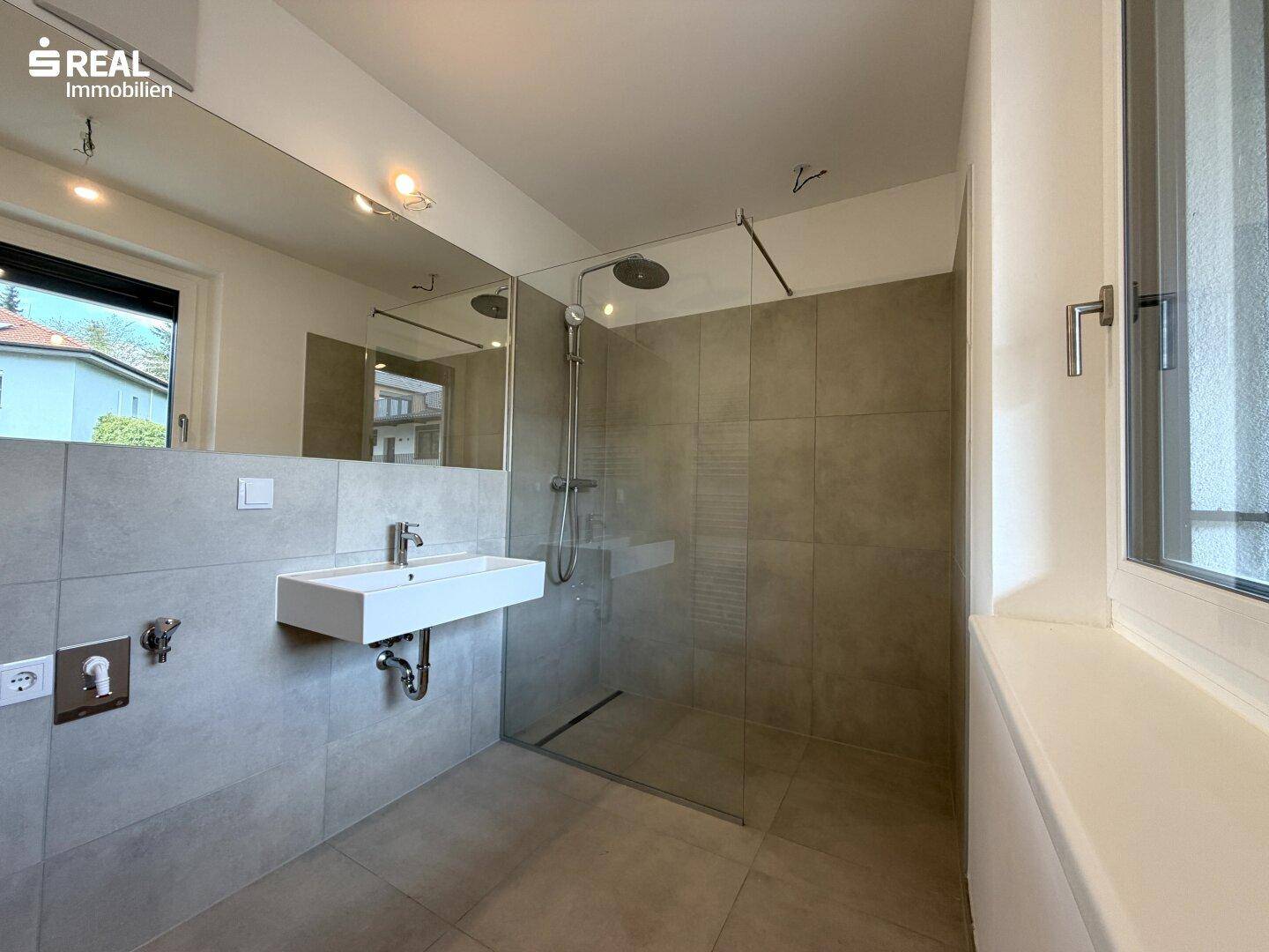 Modernes Badezimmer mit großer begehbarer Dusche, Einzelwaschbecken und großem Spiegel.