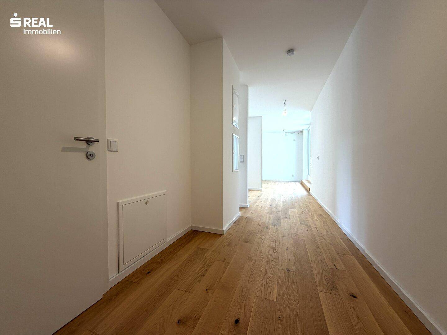 Langer, heller Flur mit Holzboden und weißen Wänden, der zu den Wohnbereichen führt.