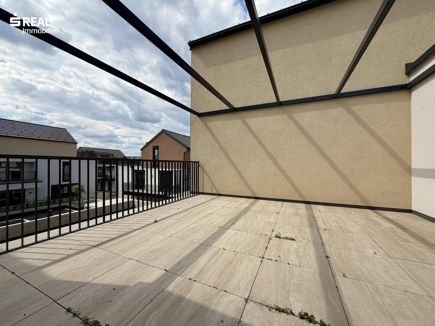 Geräumige geflieste Terrasse mit Metallgeländer und Blick auf die Nachbargebäude.
