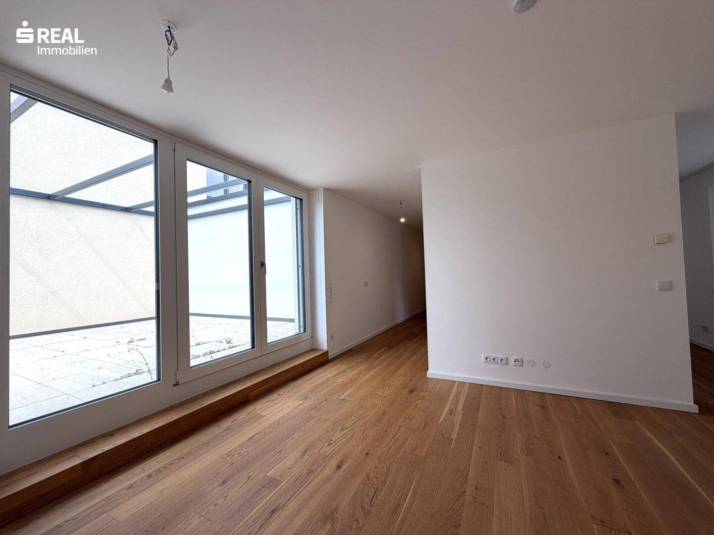 Heller Wohnbereich mit großen Fenstern, Holzboden und Zugang zu einer Terrasse.