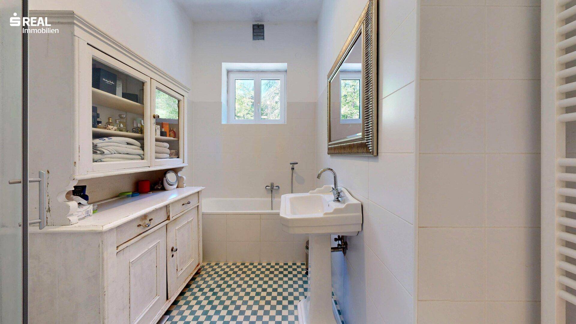 Helles Badezimmer mit Badewanne, Waschbecken und kariertem Fliesenboden.
