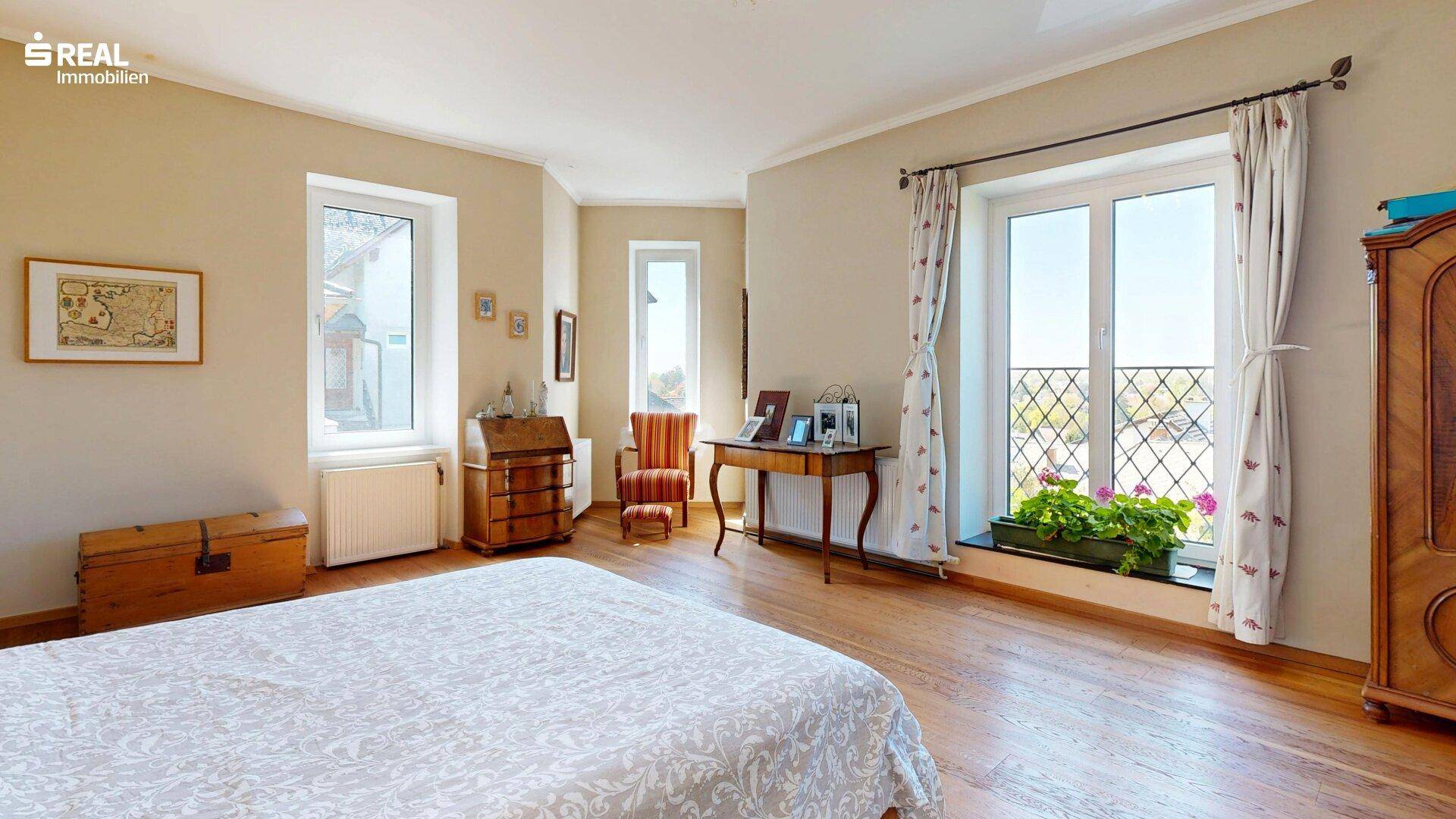 Helles Schlafzimmer mit Holzboden, mehreren Fenstern und klassischer Einrichtung.