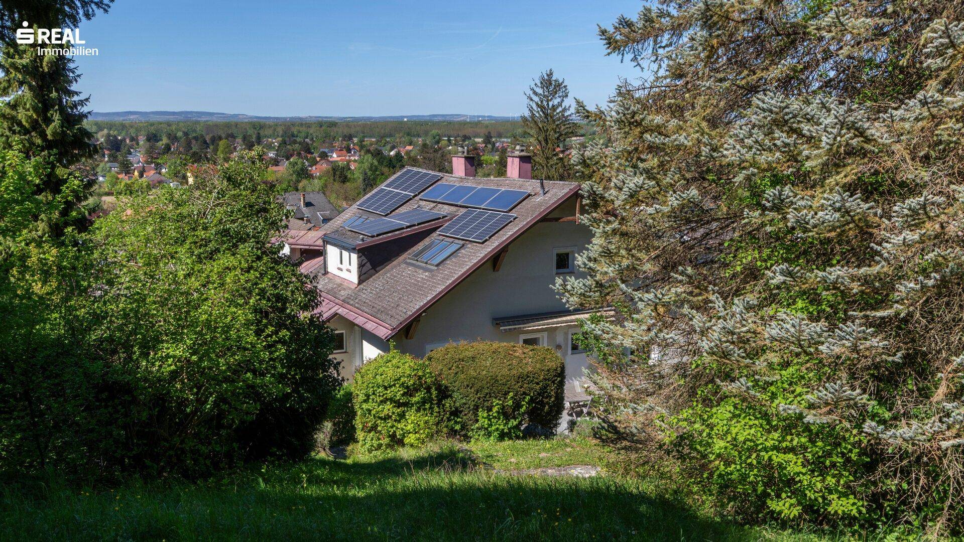 Haus mit Photovoltaikanlage auf dem Dach, umgeben von Bäumen und Weitblick.