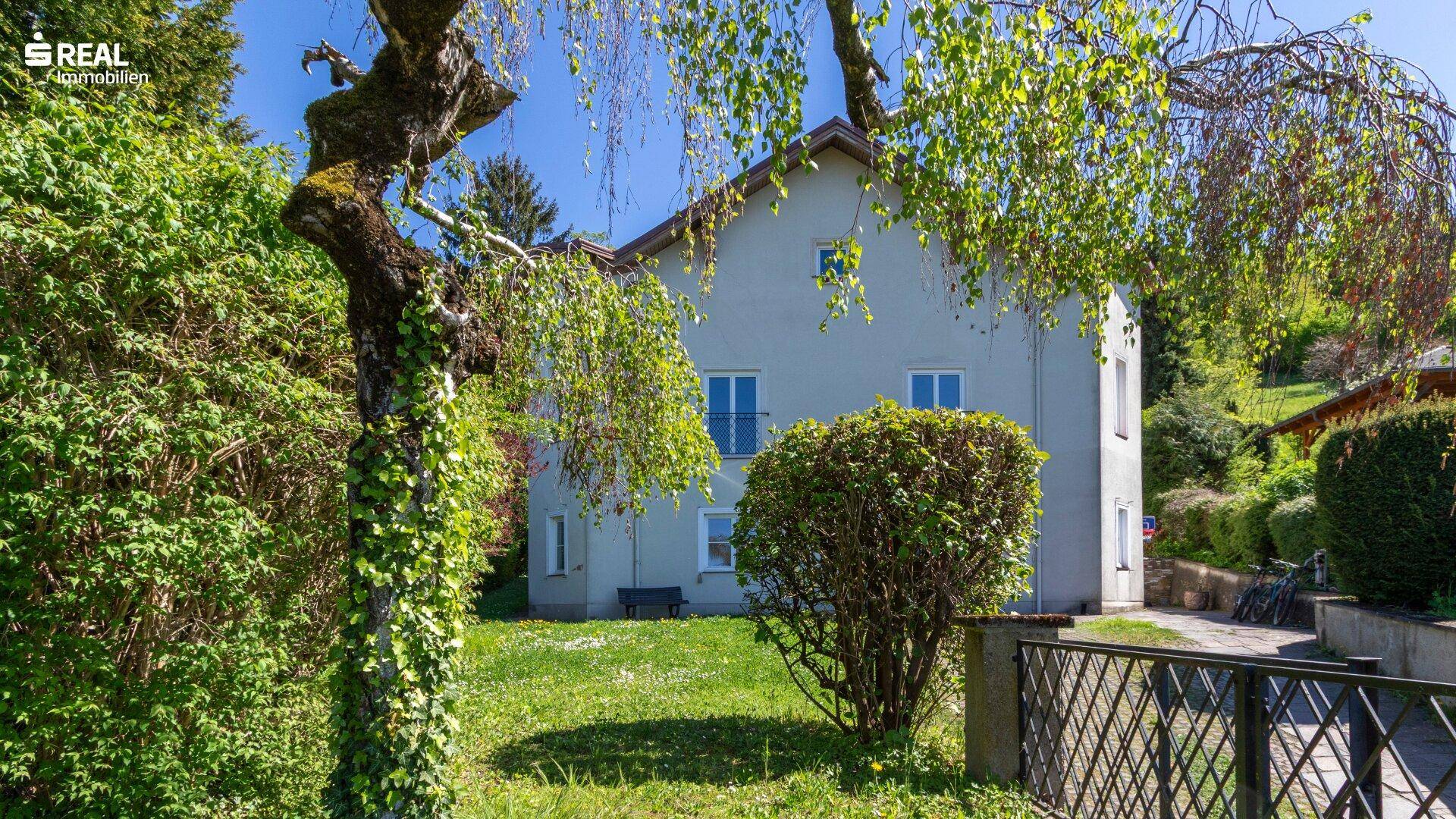 Seitenansicht des Hauses mit gepflegtem Rasen und üppiger Vegetation.