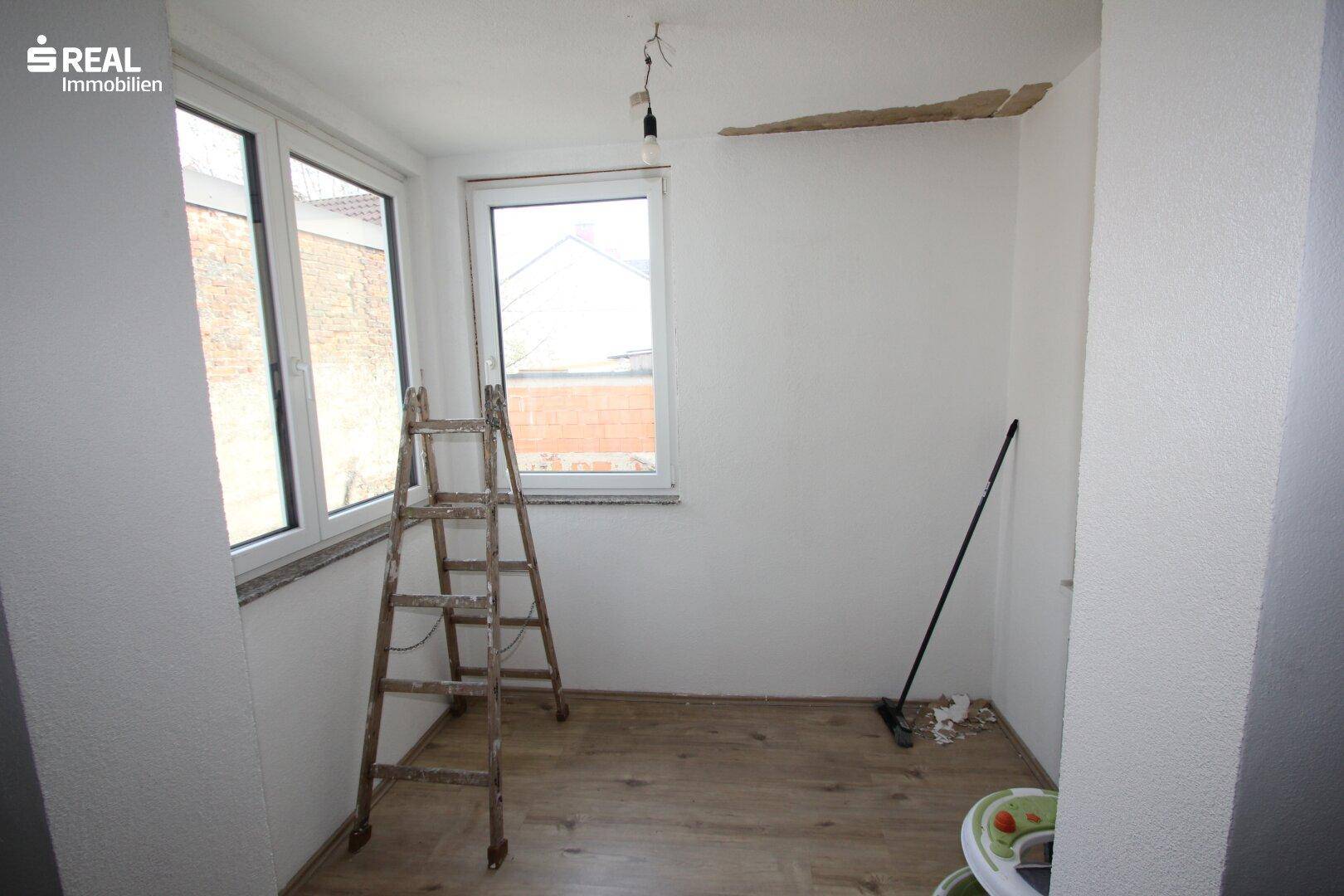 Kleiner Raum mit Fenstern, Holzboden und einer Leiter, der als Abstellraum oder Werkstatt dienen könnte.