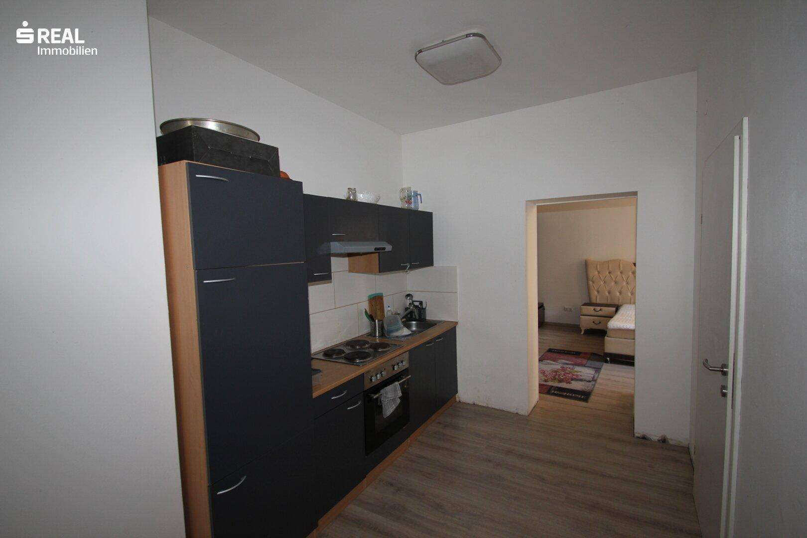 Moderne Küchenzeile mit dunklen Schränken, Herd und direktem Zugang zu einem angrenzenden Schlafzimmer.