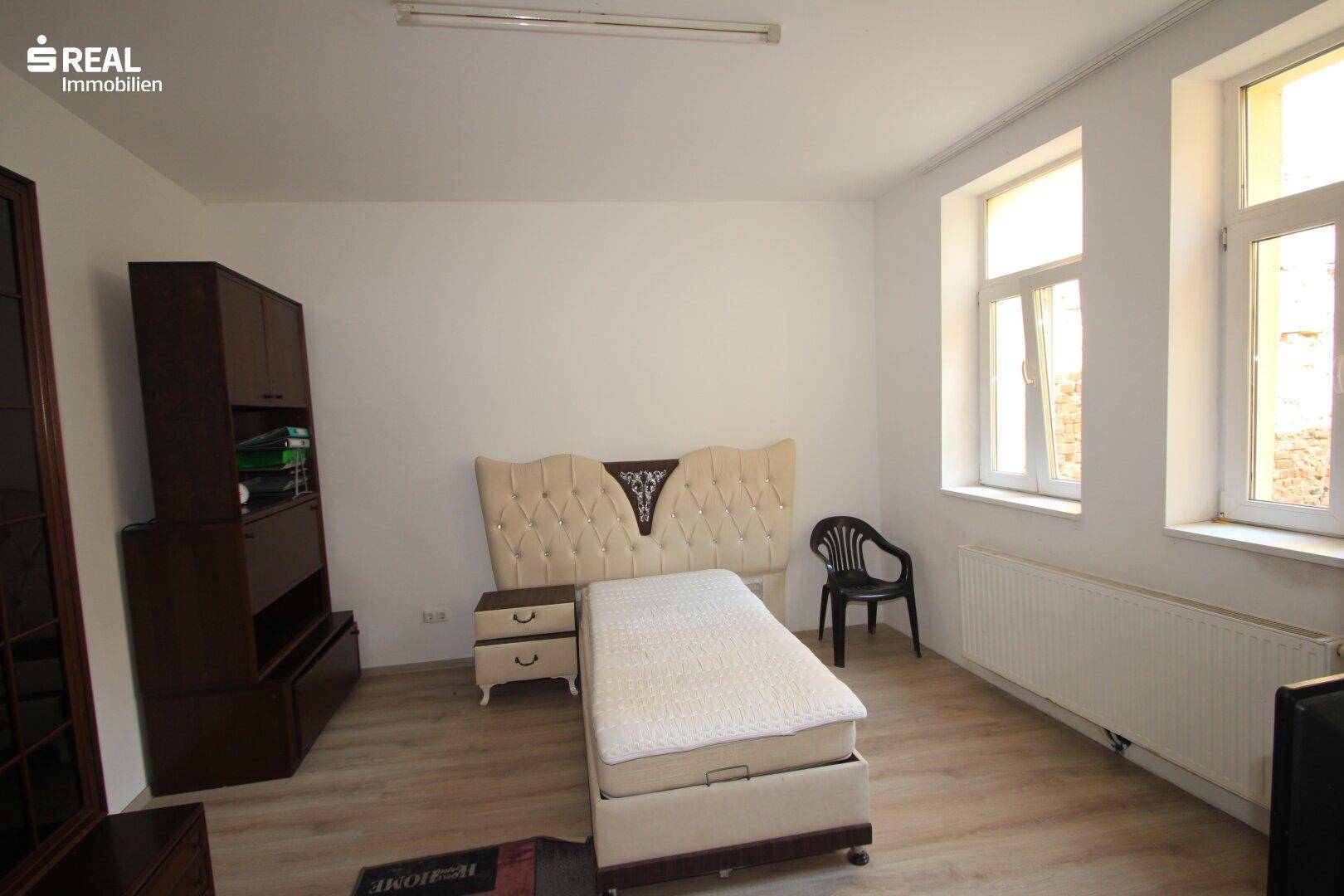 Geräumiges Schlafzimmer mit Holzboden, großem Bett mit gepolstertem Kopfteil und einem dunklen Schrank.