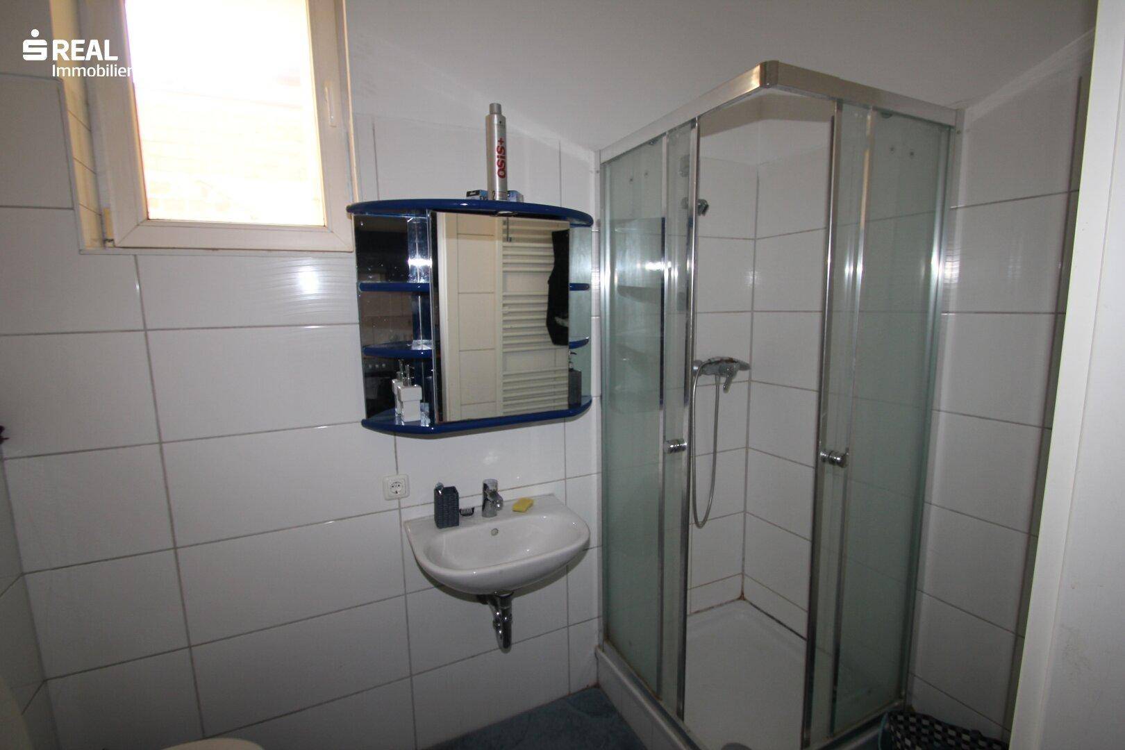 Badezimmer mit Duschkabine, Waschbecken, Spiegelschrank und einem Fenster für natürliche Belüftung.