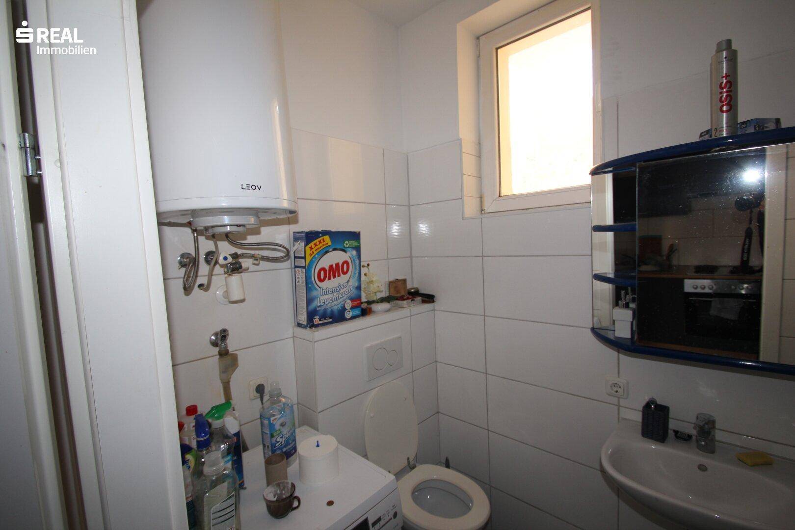Kleines Badezimmer mit WC, Waschbecken, Spiegelschrank und Warmwasserboiler, praktisch eingerichtet.