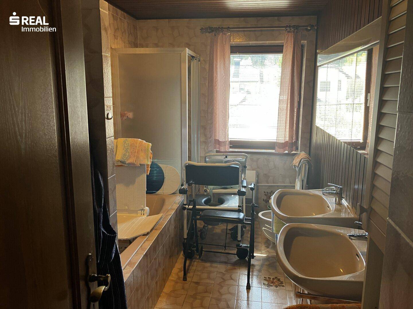 Badezimmer mit Badewanne, Dusche, Doppelwaschbecken und Haltegriffen für Barrierefreiheit.