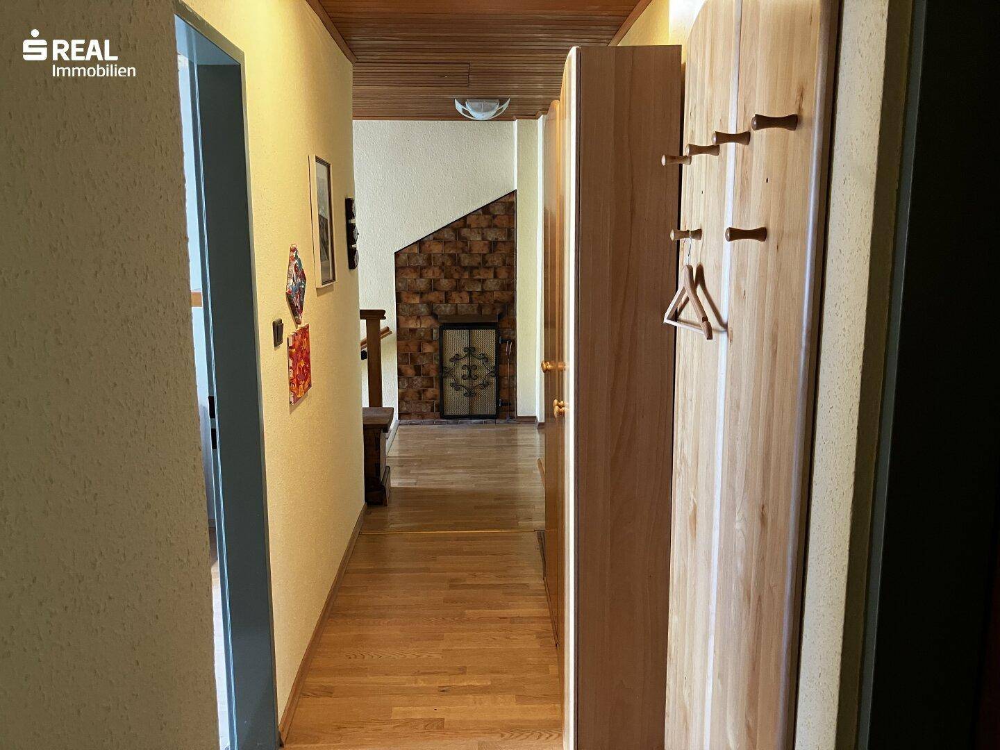 Heller Flur mit Holzfußboden und Holzdecke, führt zu einem traditionellen Kachelofen im Hintergrund.