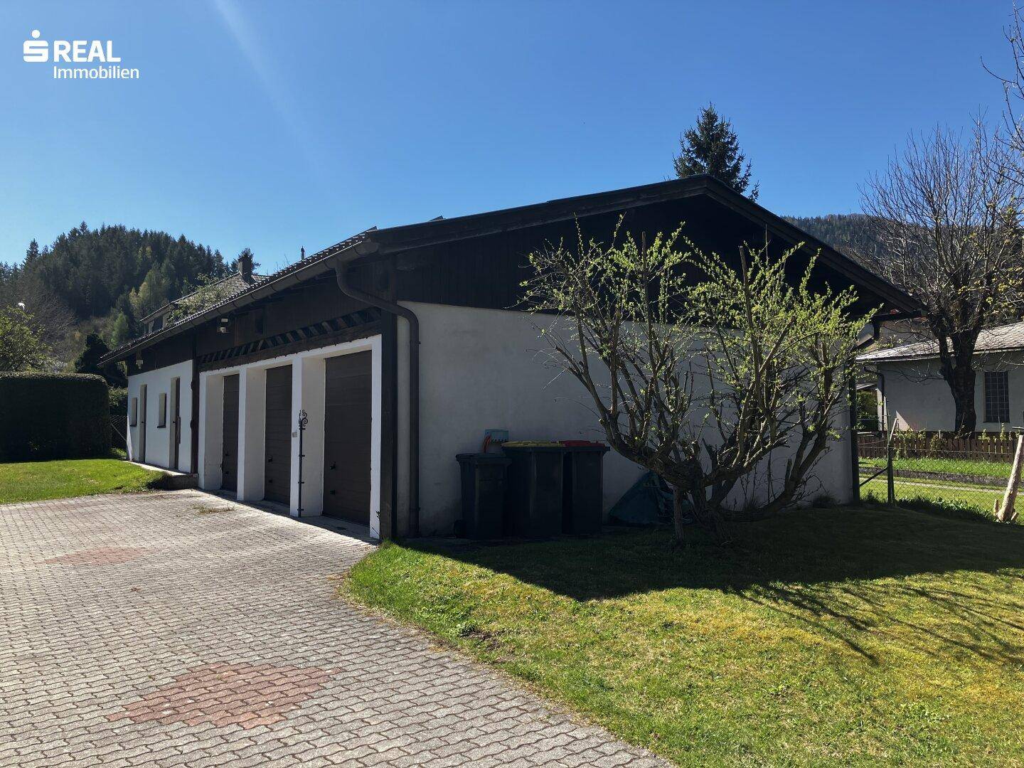 Separate Garagengebäude mit mehreren Stellplätzen und gepflasterter Zufahrt neben dem Haupthaus.