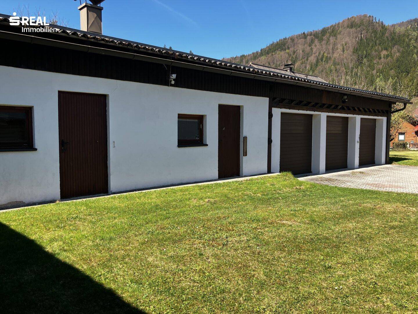 Nahaufnahme der Garagenfront mit mehreren Toren und einem gepflegten Rasenbereich davor.