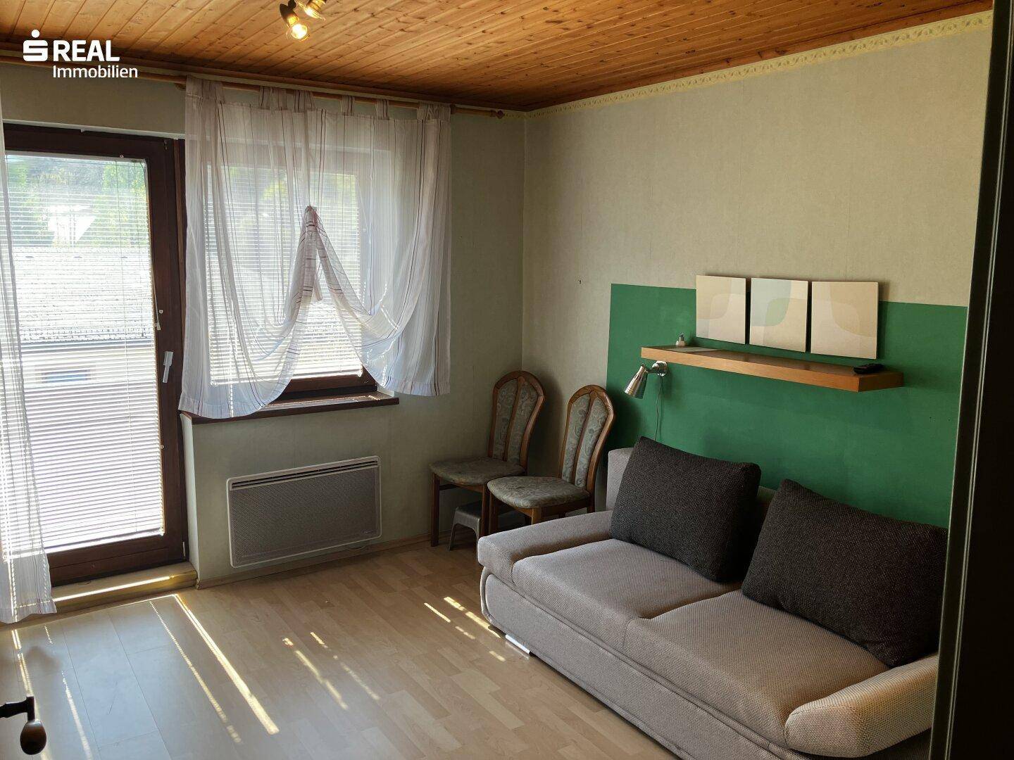 Helles Zimmer mit Schlafsofa, Holzboden und Zugang zu einem Außenbereich durch eine Glastür.