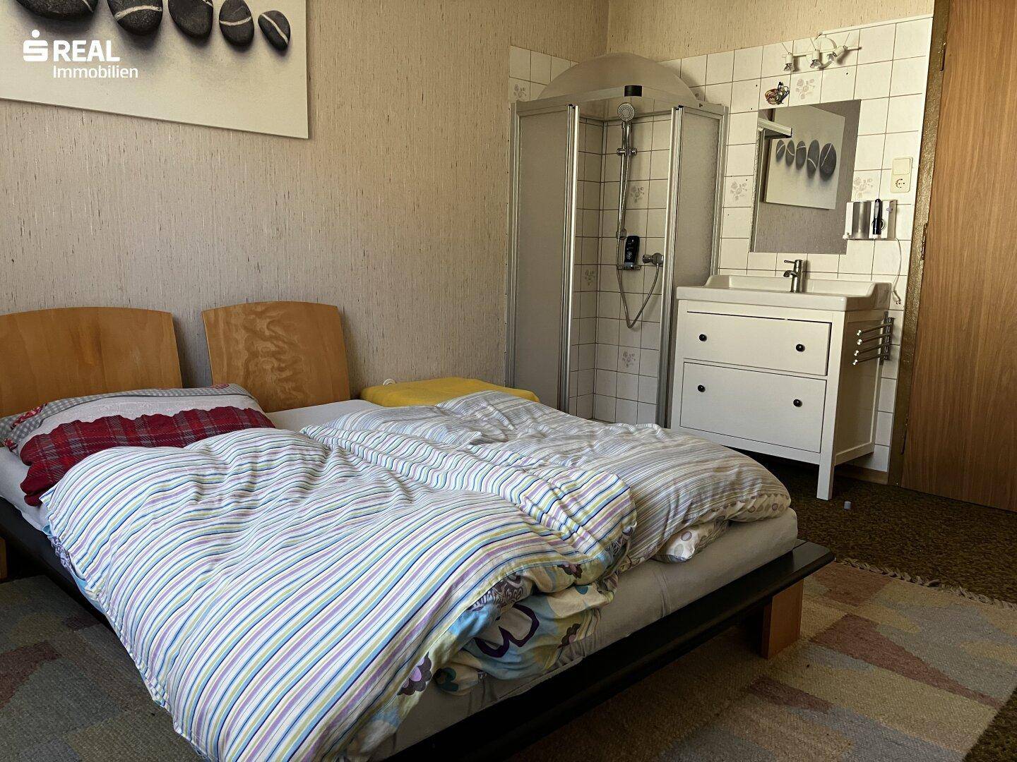 Schlafzimmer mit Doppelbett, integriertem Waschbecken und Duschkabine, mit Teppichboden.
