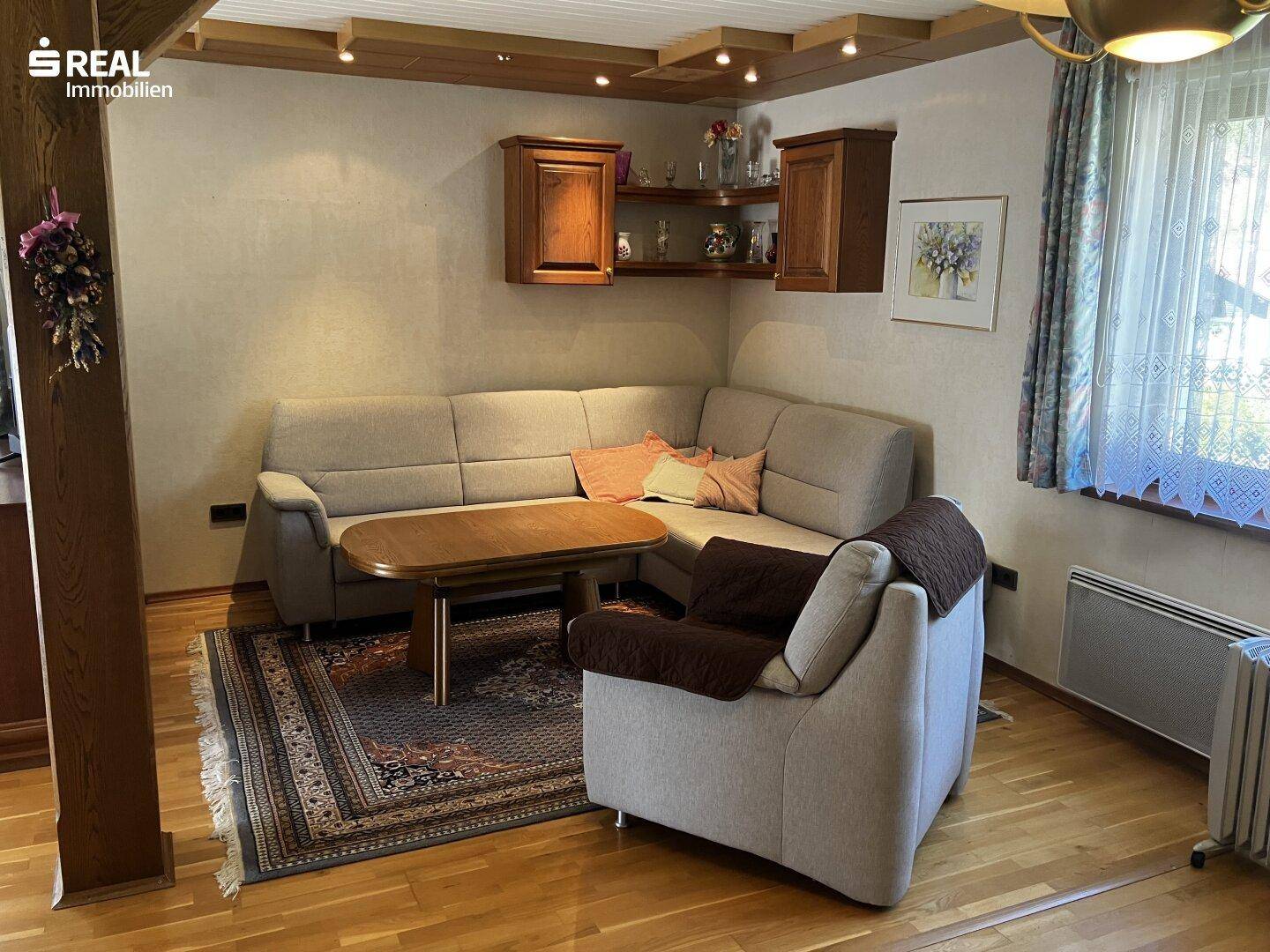 Gemütliches Wohnzimmer mit Ecksofa, Holztisch und Holzdecke, ausgestattet mit Teppich und Vorhängen.