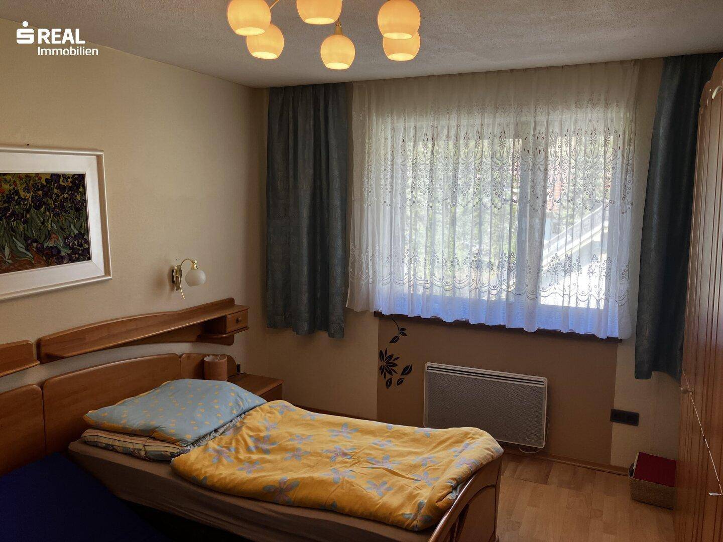 Schlafzimmer mit Doppelbett, Holzmöbeln und großem Fenster, das viel Tageslicht hereinlässt.