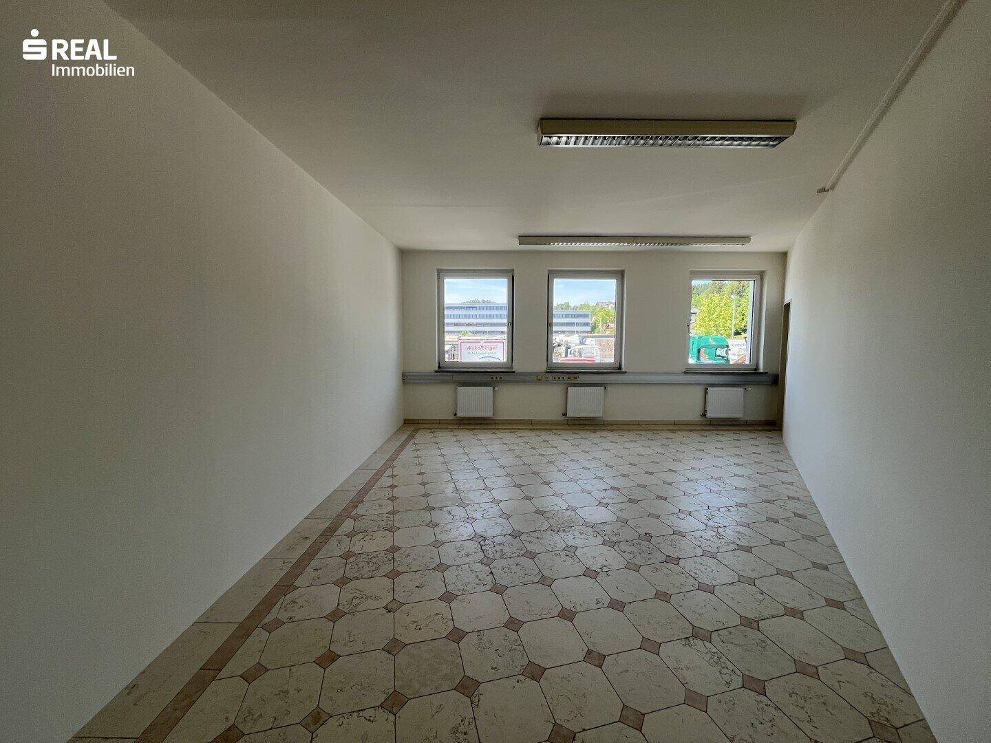 Heller Büroraum mit gefliestem Boden und Blick auf die Umgebung durch die Fenster.