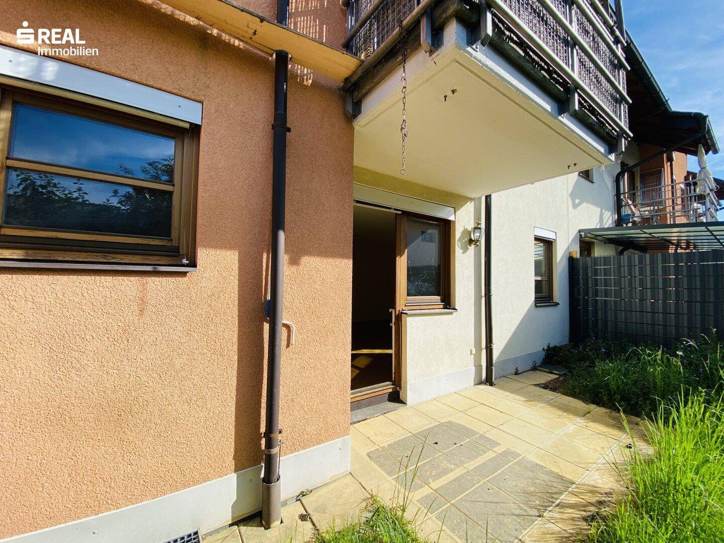 Außenbereich mit gepflasterter Terrasse und Zugang zum Garten, unter einem Balkon gelegen.
