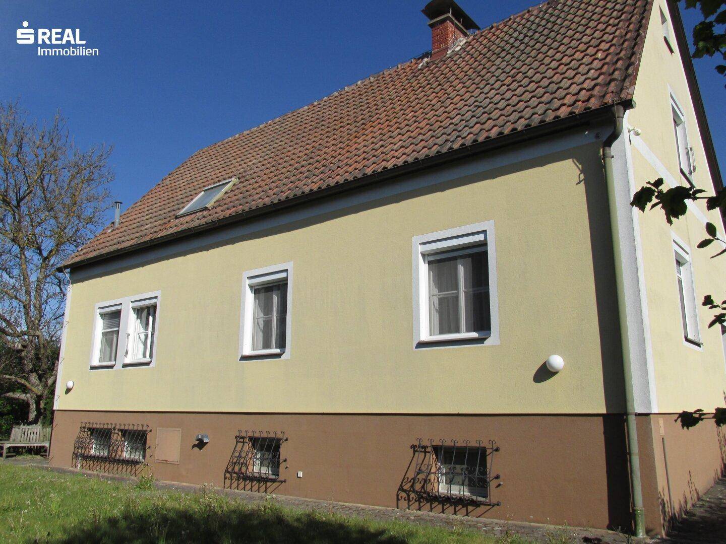 Seitenansicht des Hauses mit gelber Fassade, braunem Sockel und vergitterten Kellerfenstern.