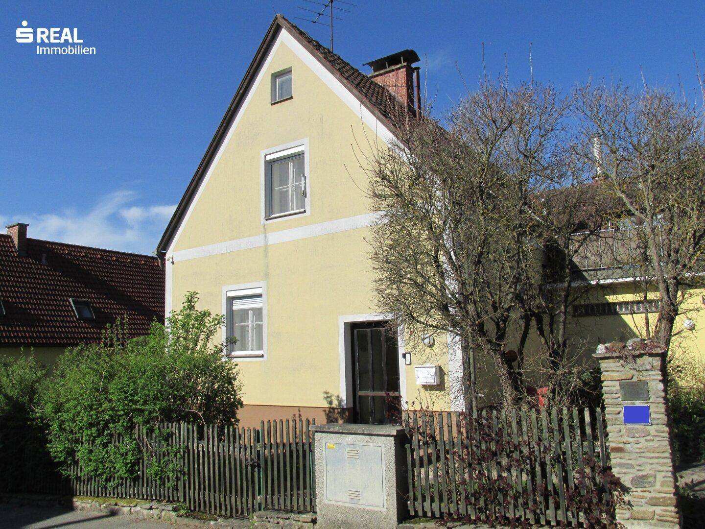 Vorderansicht des Einfamilienhauses mit gelber Fassade, Holzzaun und gepflegtem Vorgarten.