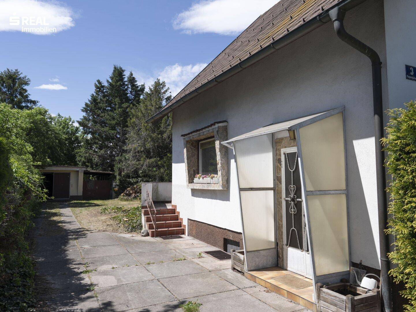 Seitenansicht des Hauses mit überdachtem Eingangsbereich und Zufahrt zum hinteren Grundstück.