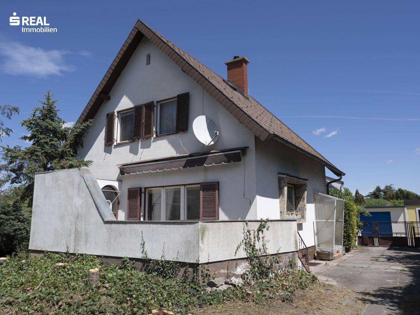 Rückansicht des Hauses mit Fensterläden und einem kleinen Anbau, umgeben von Vegetation.