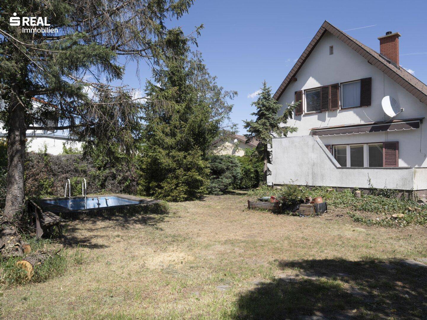 Gartenbereich mit Rasenfläche, hohen Bäumen und einem kleinen, eingelassenen Pool neben dem Haus.