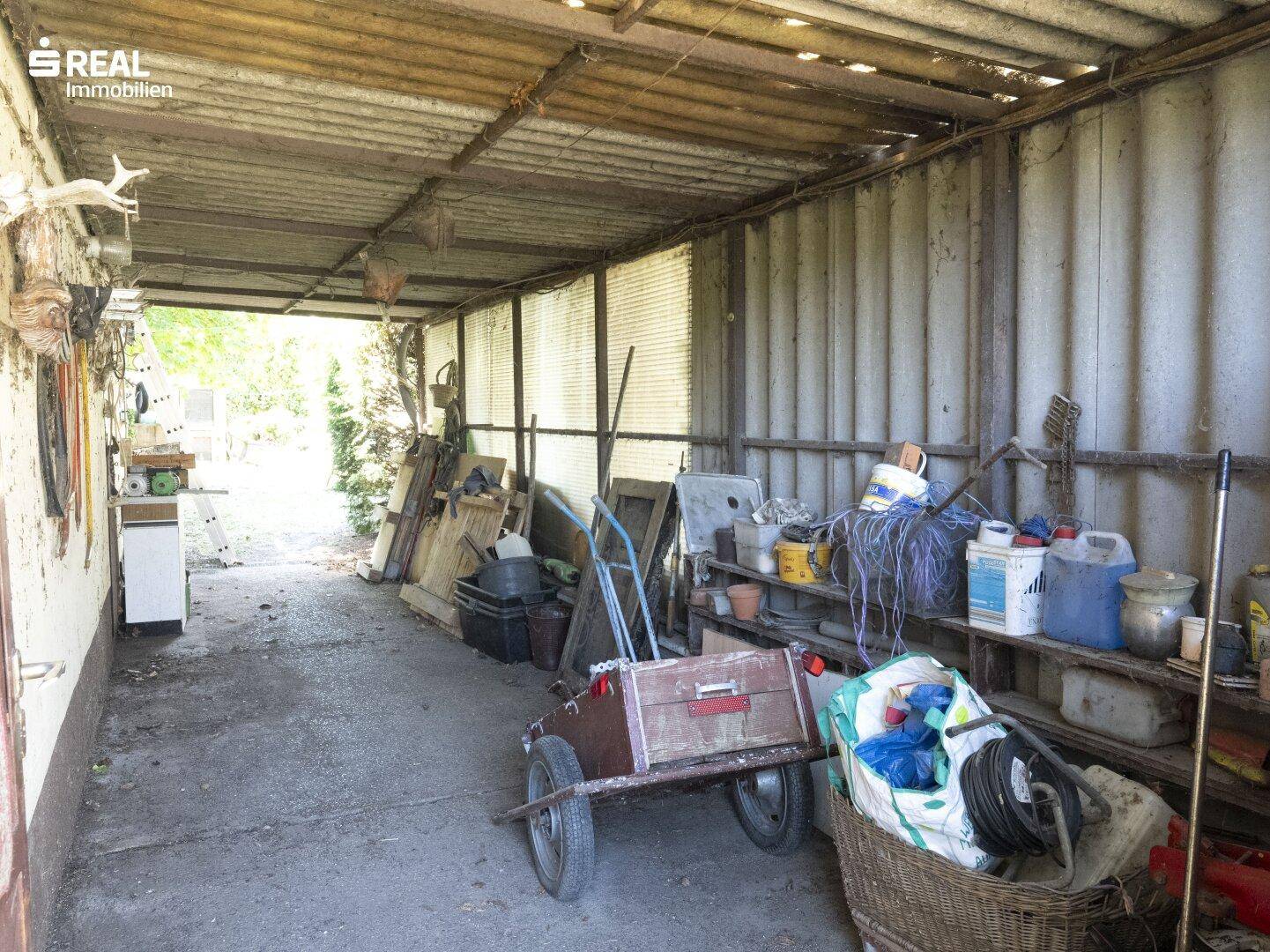 Überdachter Bereich, genutzt als Lager oder Werkstatt, mit vielen Utensilien und Materialien.