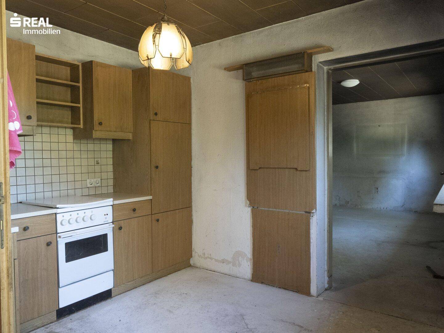 Einfache Küche mit Holzschränken, einem alten Herd und Fliesen an der Wand, bereit zur Renovierung.