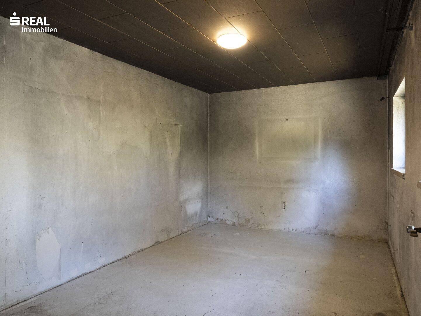 Leerer Raum mit unverputzten Wänden und einfacher Deckenbeleuchtung, bereit für den Ausbau.