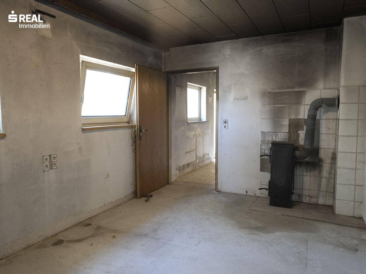 Leerer Raum mit einem Holzofen und Fenstern, ideal für eine zukünftige Nutzung nach Renovierung.