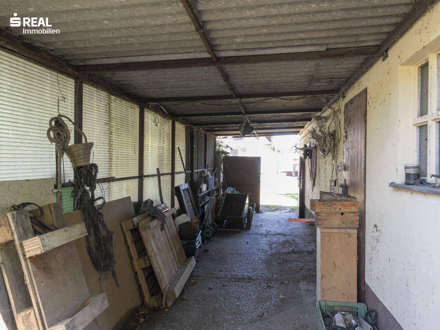 Überdachter Bereich, genutzt als Lager oder Werkstatt, mit vielen Utensilien und Materialien.