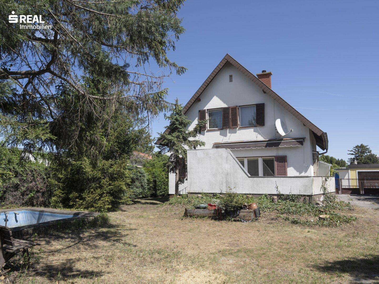Gartenbereich mit Rasenfläche, hohen Bäumen und einem kleinen, eingelassenen Pool neben dem Haus.