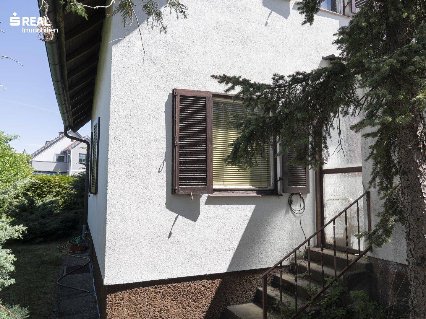Seitenansicht des Hauses mit einem Fenster mit Jalousien und einer Außentreppe.