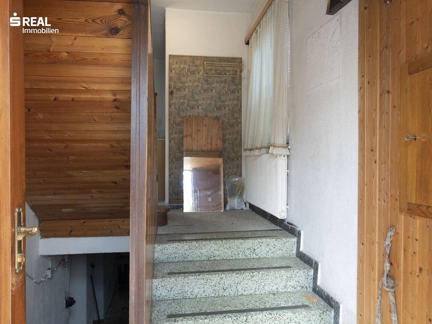 Eingangsbereich mit Holzvertäfelung, Terrazzostufen und Blick in den Keller.