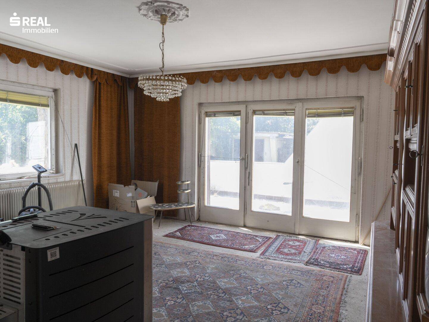 Geräumiges Wohnzimmer mit Kaminofen, Kronleuchter und Zugang zu einer Außentür.
