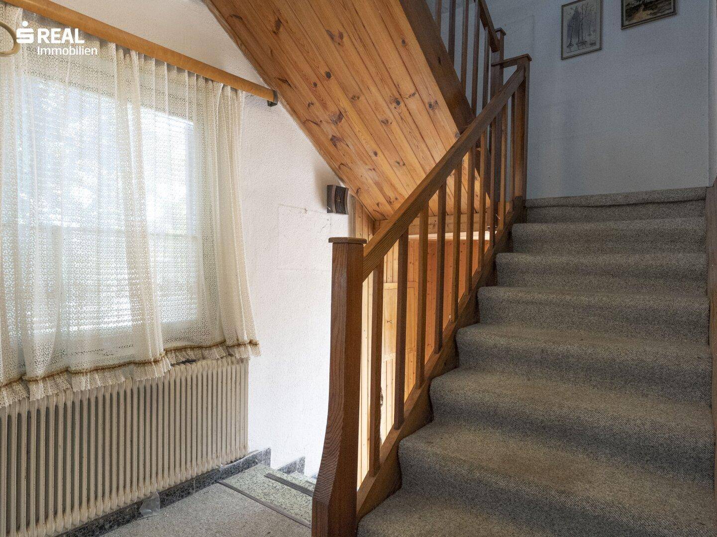 Treppenhaus mit Holzgeländer und Teppichboden, das in die obere Etage führt.