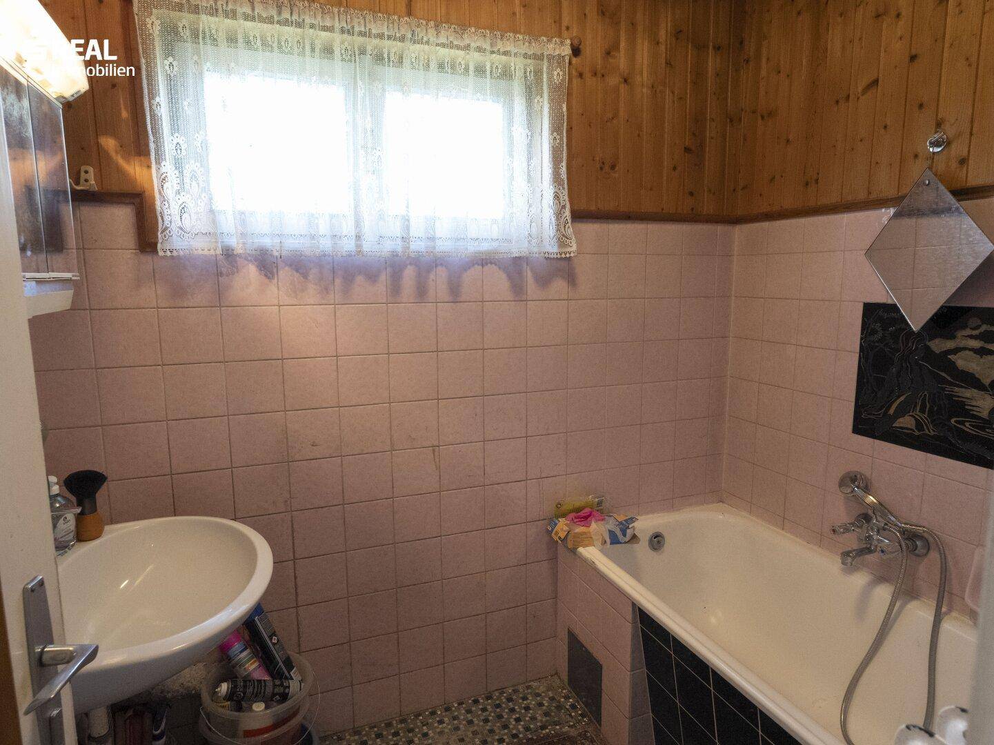 Badezimmer mit rosa Fliesen, Waschbecken, Badewanne und Holzvertäfelung an der Wand.