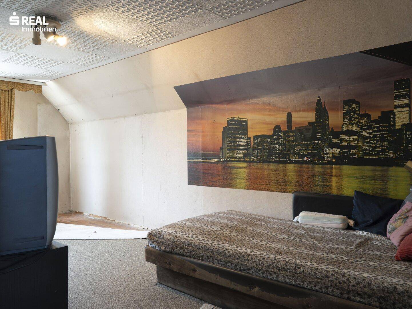 Schlafzimmer im Dachgeschoss mit Bett, Stadtbild-Wandgemälde und schräger Decke.