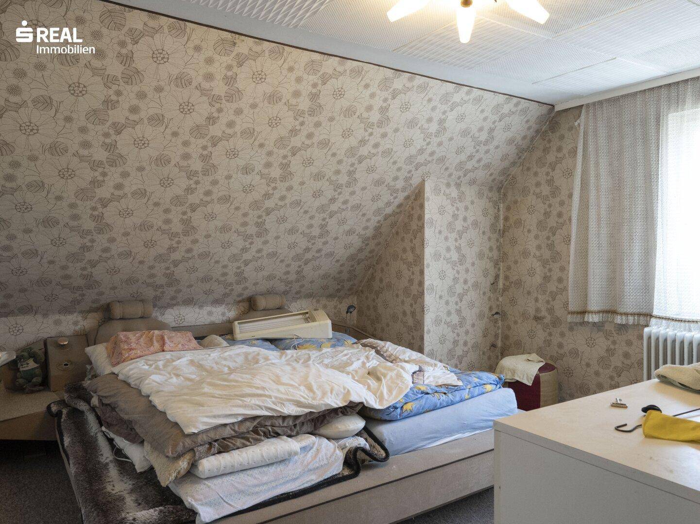 Schlafzimmer im Dachgeschoss mit Bett, gemusterter Tapete und schräger Decke.